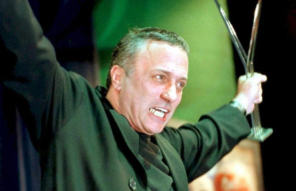 Picture of a man at an award ceremony. He is standing on a stage with both arms raised in the air. In one hand he holds a trophy. He is the Israeli actor and director Assaf Dayan, who appears to be receiving an award at the moment the photograph is taken.