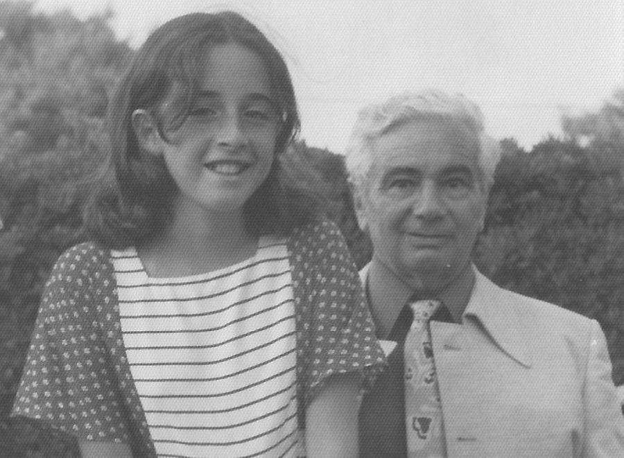 Black and white photograph of an elderly man and a young girl. The grey-haired man, Heinz Katzenstein, is dressed in a formal shirt, jacket and tie. In front of him stands a young girl, his granddaughter Miki, in a short-sleeved patterned dress. Both look directly into the camera.